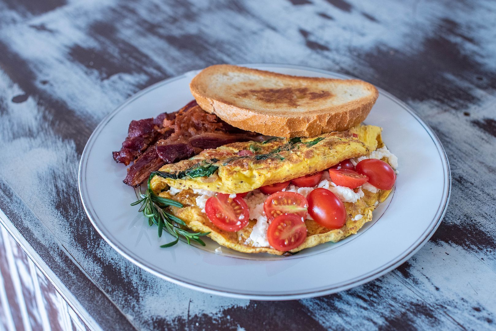 A white plate topped with an omelet , tomatoes , bacon and toast.