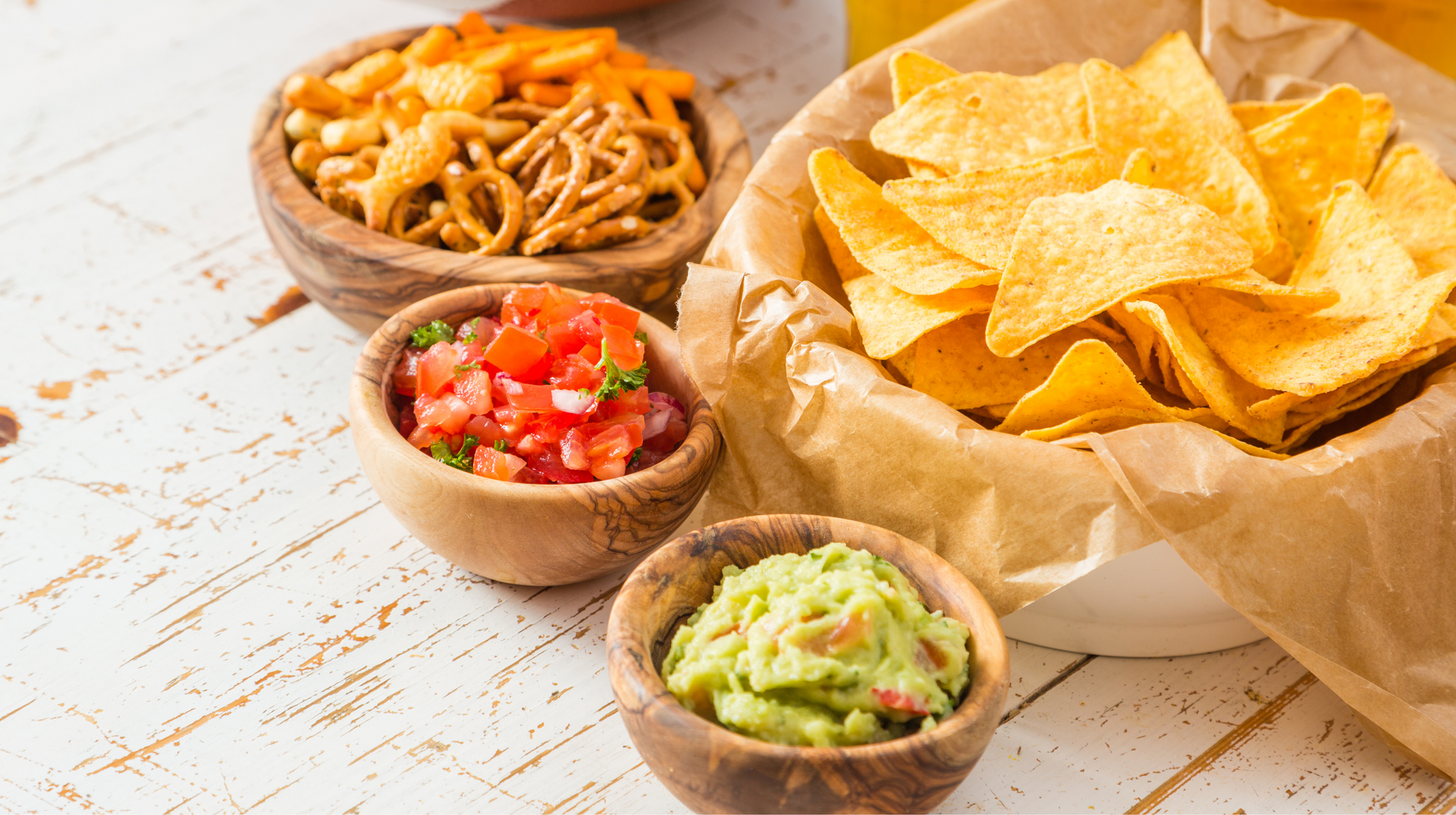 A bowl of tortilla chips , guacamole , and other snacks on a table.