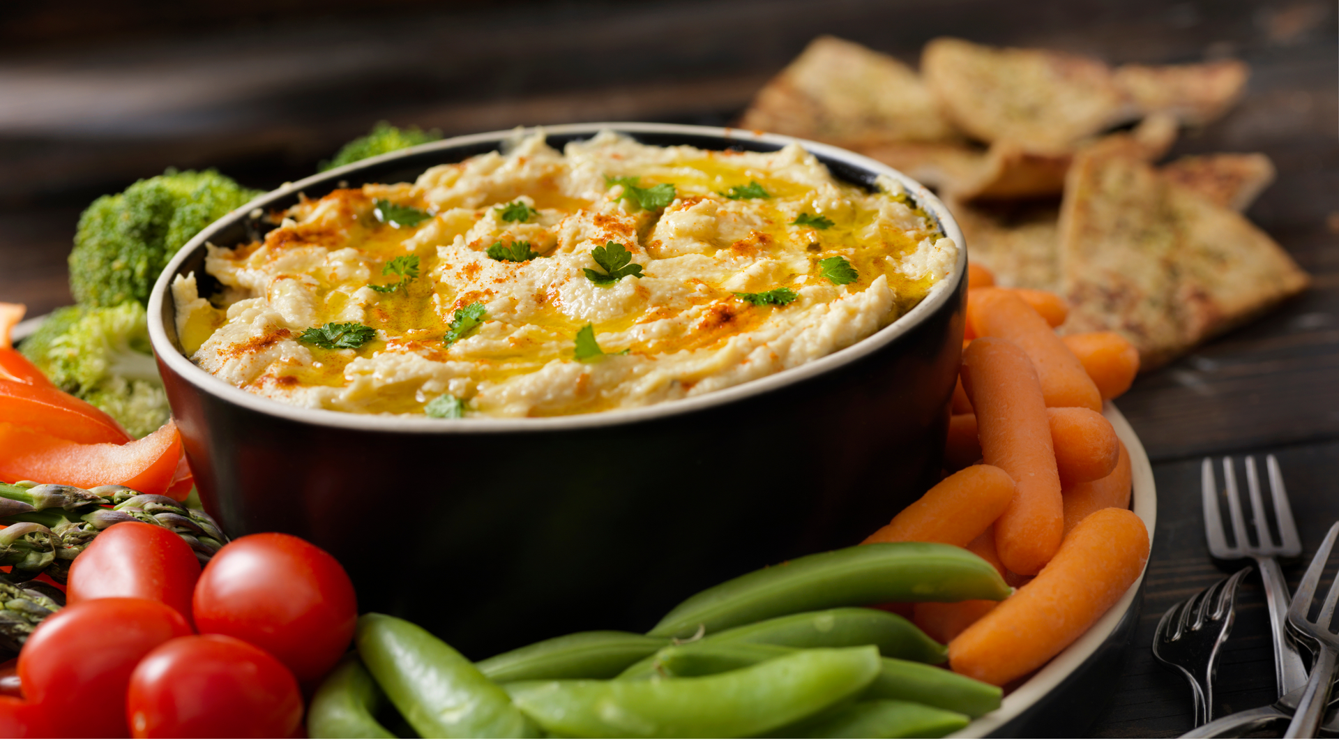 A bowl of dip surrounded by vegetables on a plate.