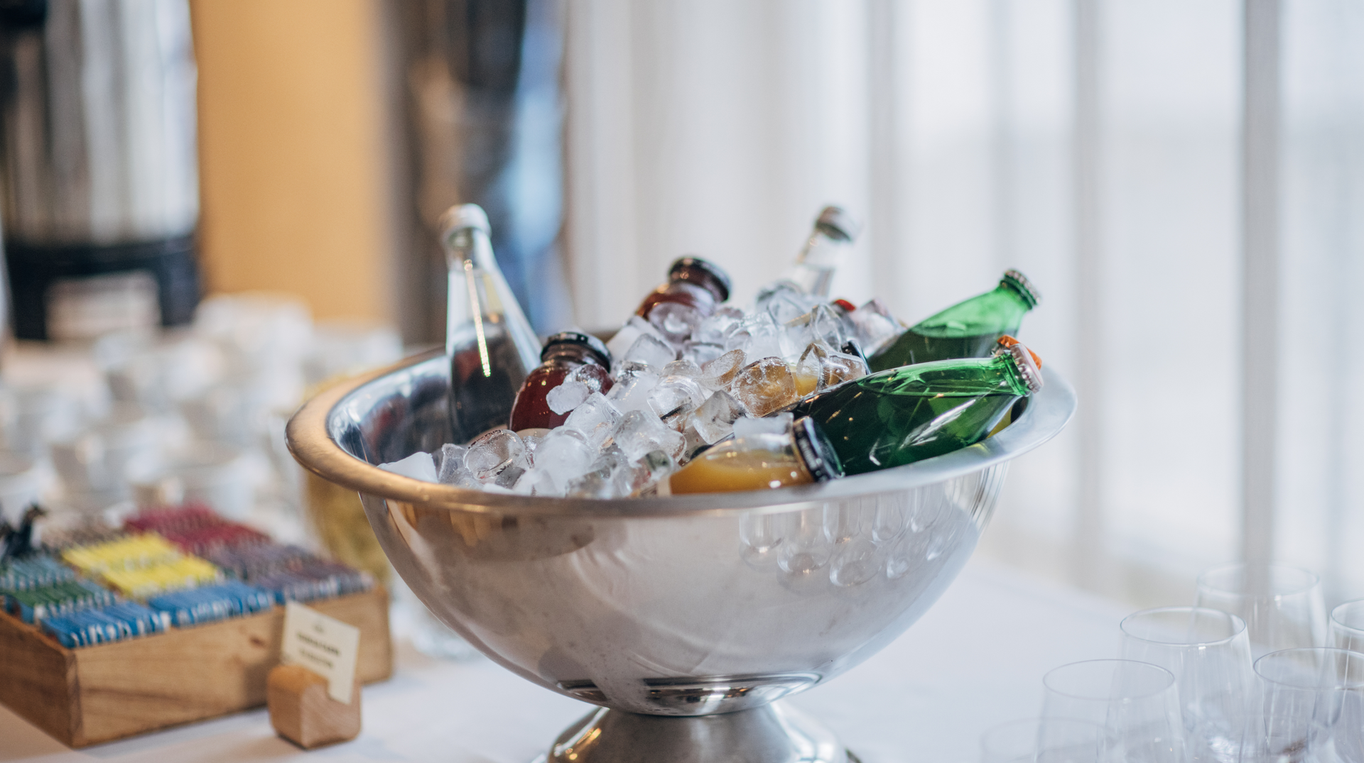 A metal bowl filled with ice and bottles of beer on a table.