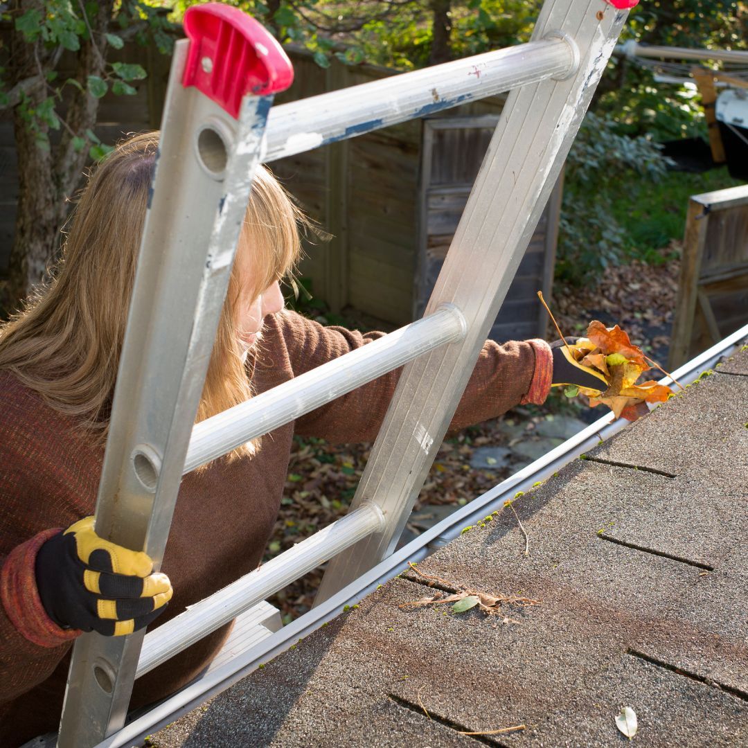a woman is using a ladder to remove leaves from a roof