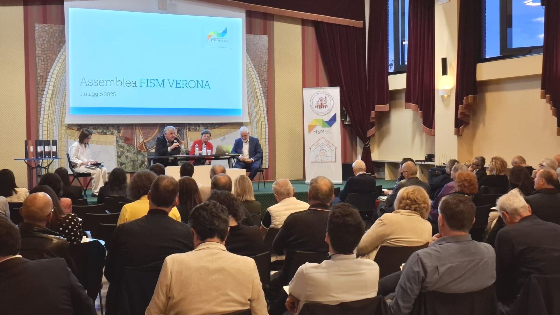 Un folto gruppo di persone è seduto davanti allo schermo di un proiettore.
