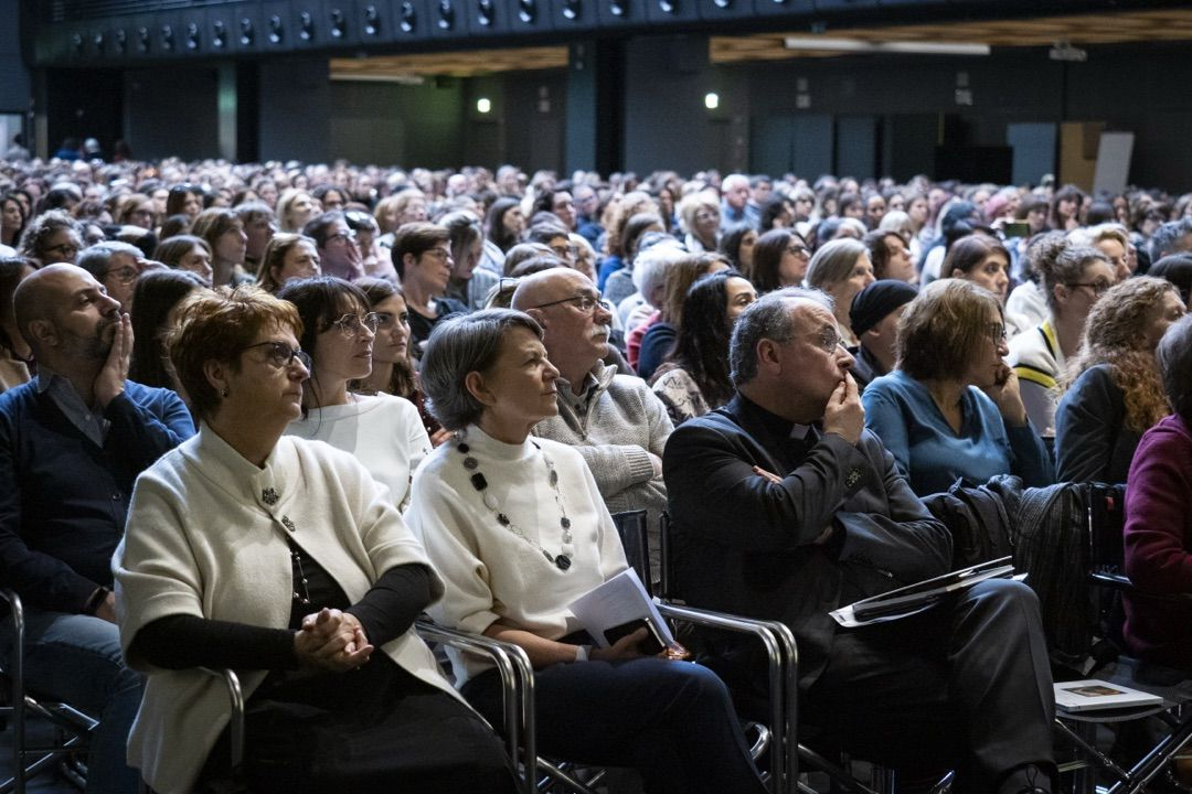 Una donna tiene in mano un microfono davanti a una folla di persone in un auditorium.