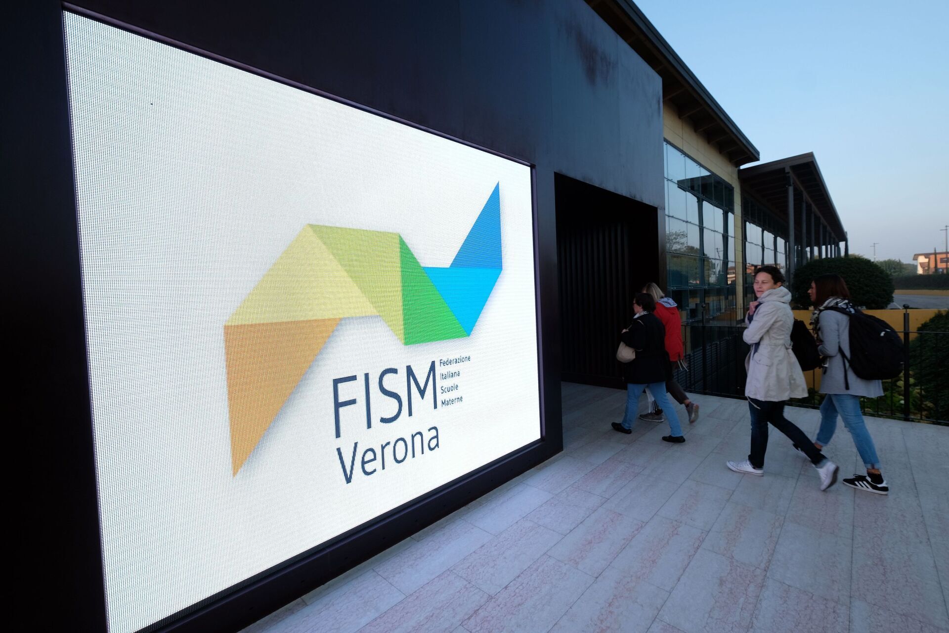 Un gruppo di persone cammina davanti ad un maxischermo con su scritto fisme verona.