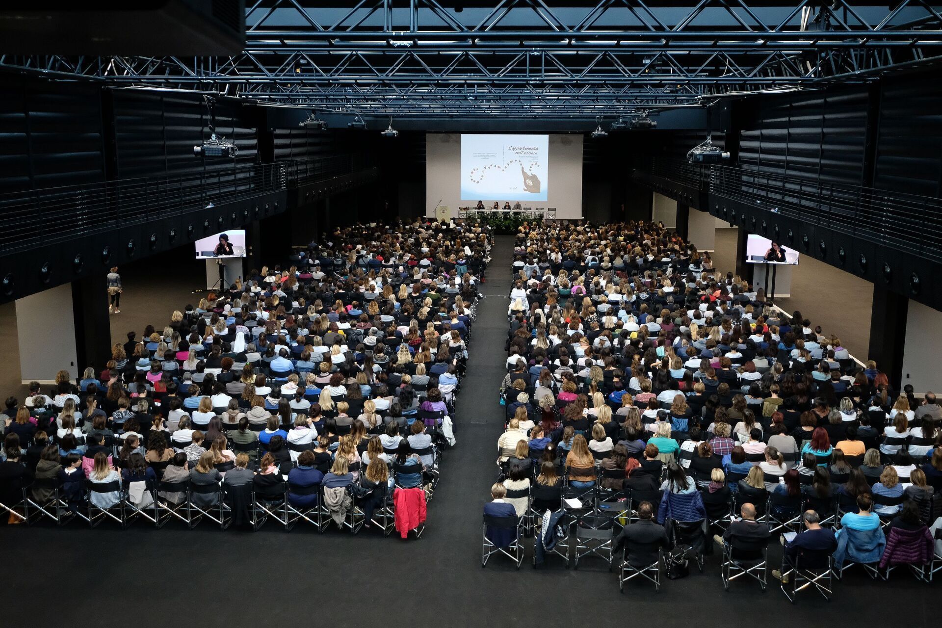 Un folto gruppo di persone è seduto in un grande auditorium e guarda una presentazione.
