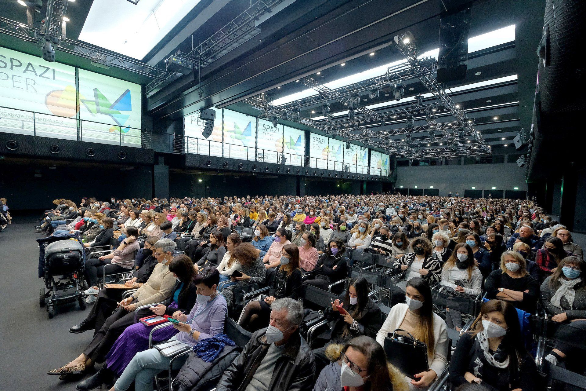 Un folto gruppo di persone è seduto in un grande auditorium.