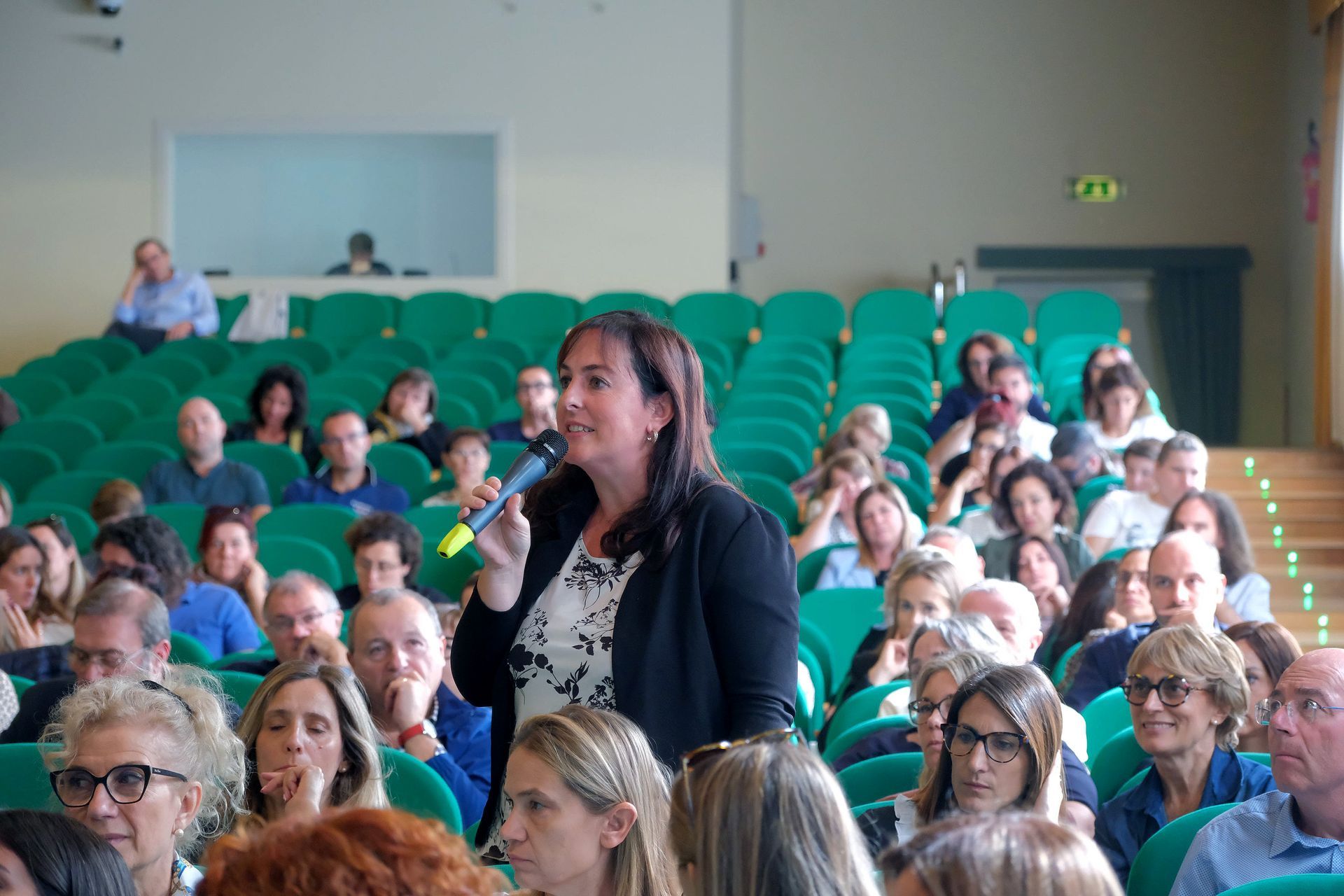 Una donna tiene in mano un microfono davanti a una folla di persone in un auditorium.