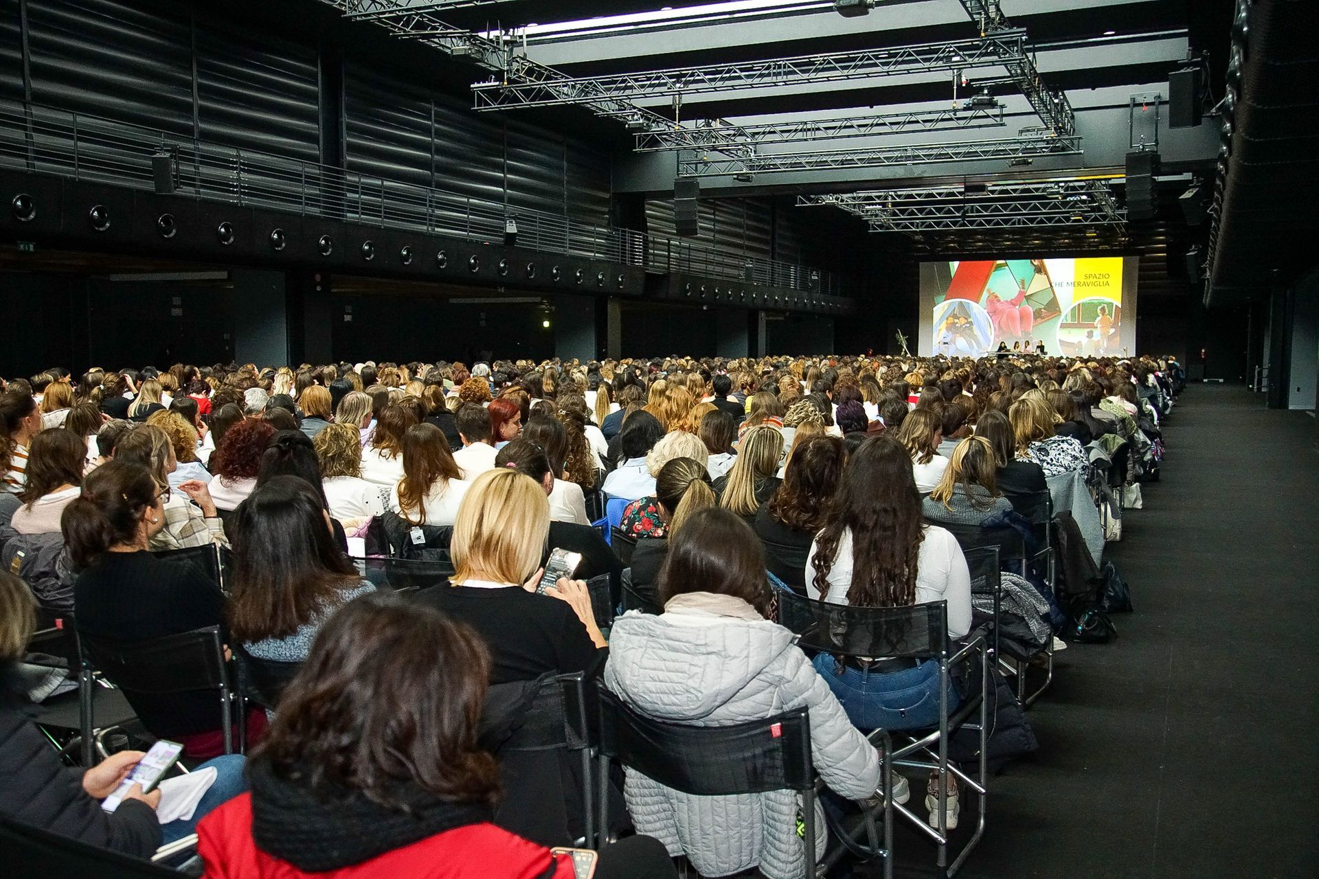 Una donna tiene in mano un microfono davanti a una folla di persone in un auditorium.