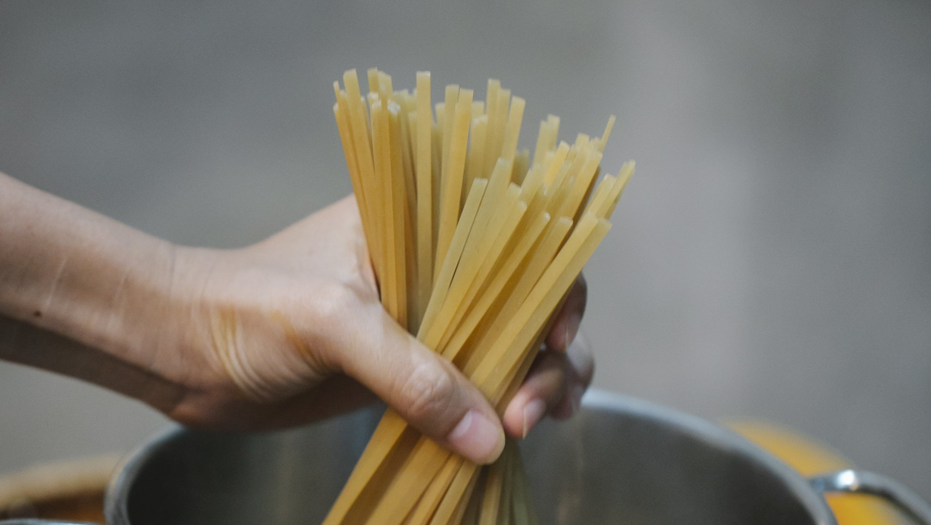 Una persona tiene in mano un mazzo di spaghetti sopra una pentola d'acqua.
