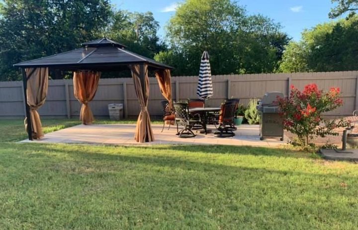 Backyard patio with gazebo, table, umbrella, grill, and grass.