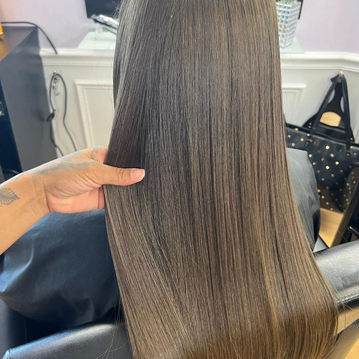 A woman is sitting in a chair holding her hair after her keratin treatment