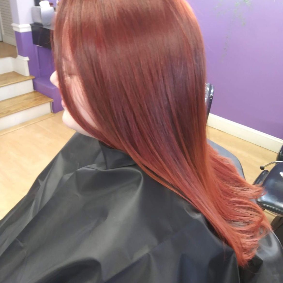A woman with long red hair is getting her hair cut