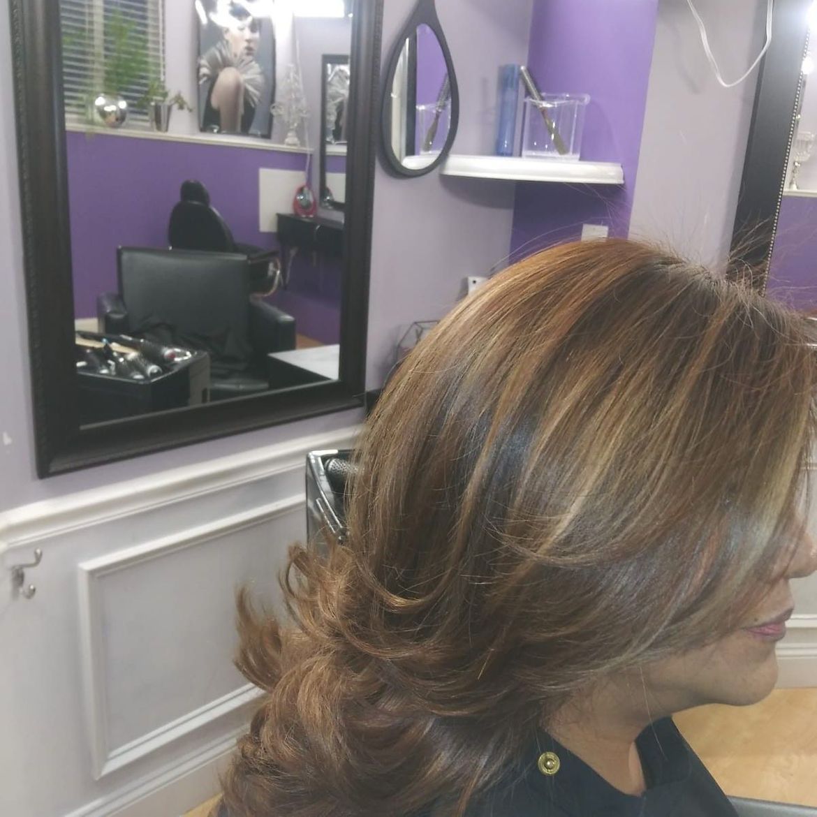 A woman is sitting in front of a mirror in a salon showing her blow dried hair.
