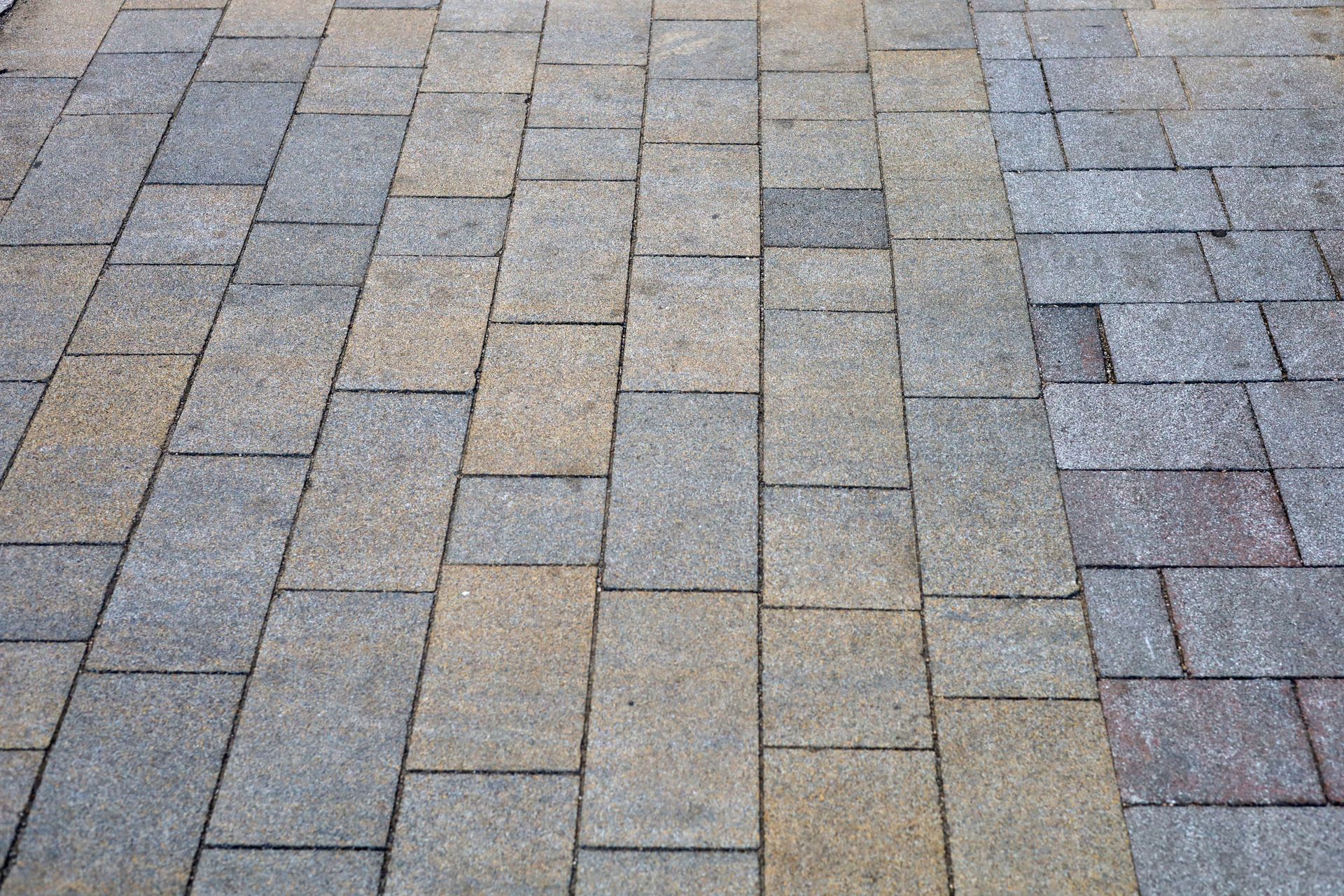 Gray and tan brick pavement laid in a staggered pattern, viewed from above