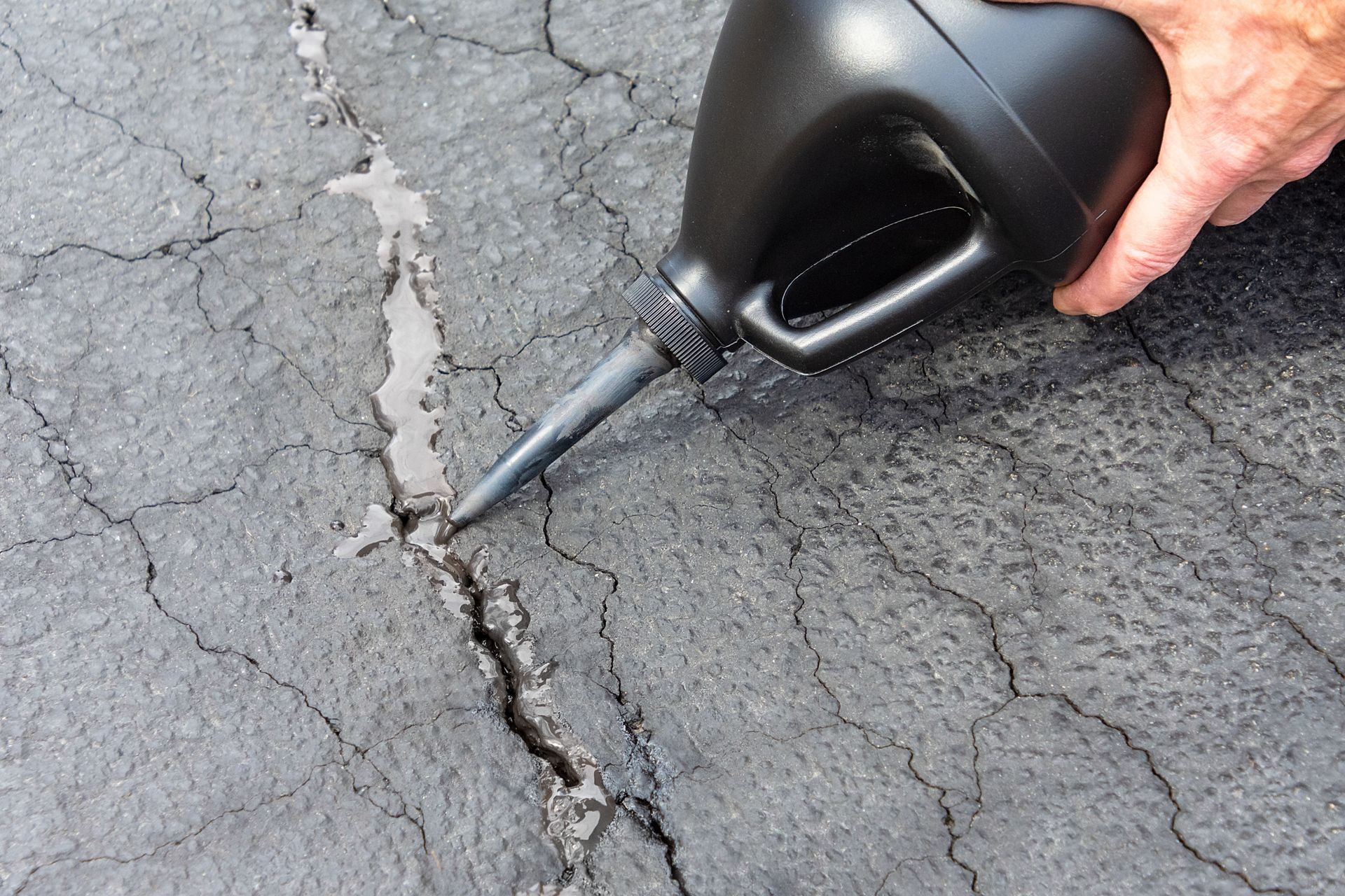 Hand pouring black sealant into a crack in asphalt pavement