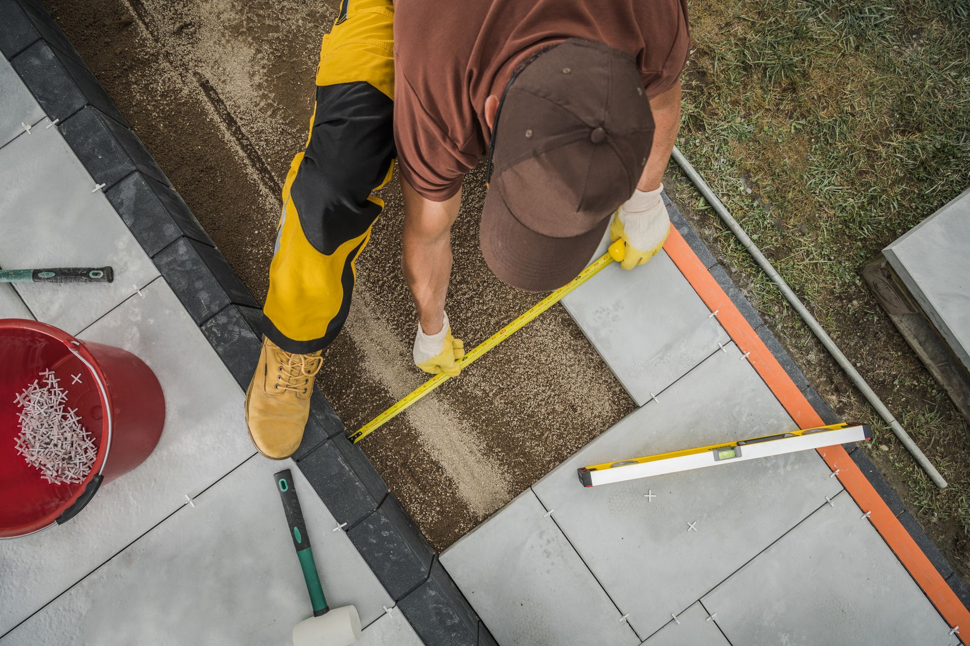 Worker measuring paving stones beside a tiled walkway with a tape measure and straightedge