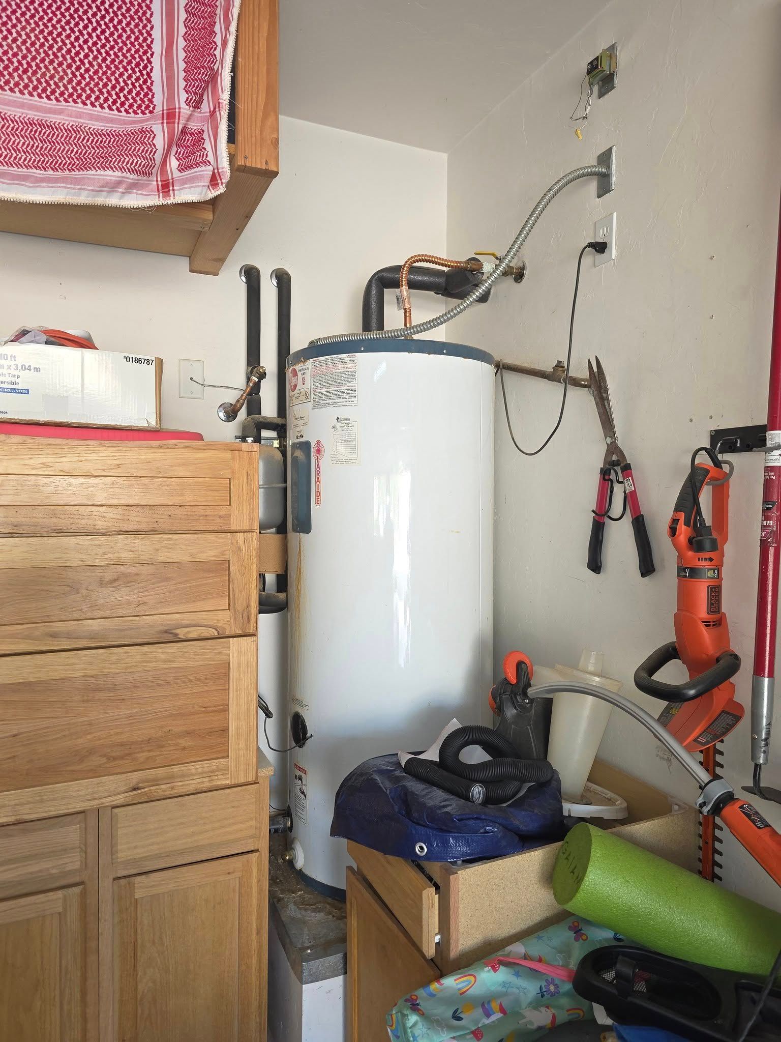 Water heater in a corner, surrounded by tools and storage.