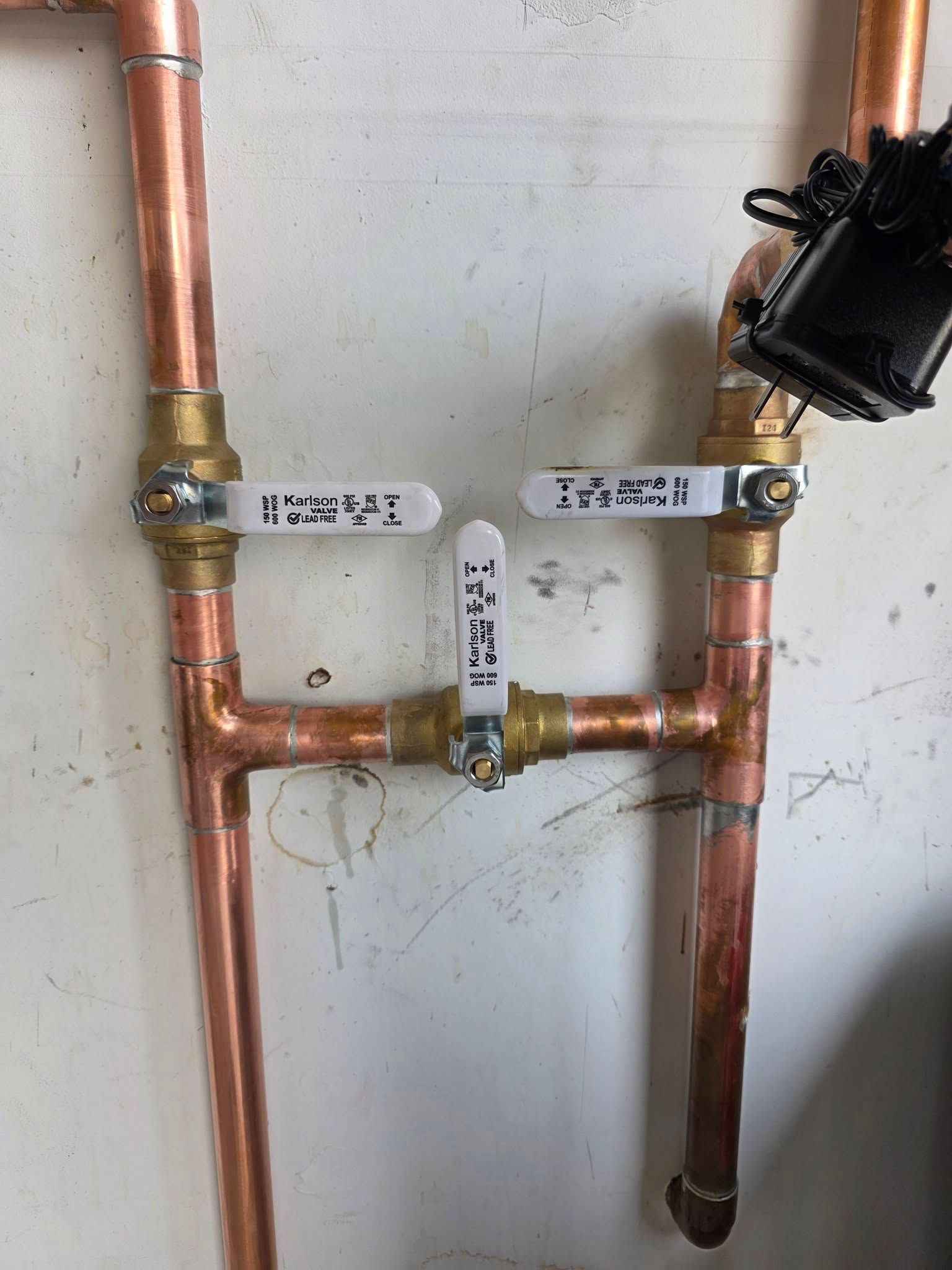 Copper plumbing pipes with three white-handled ball valves.