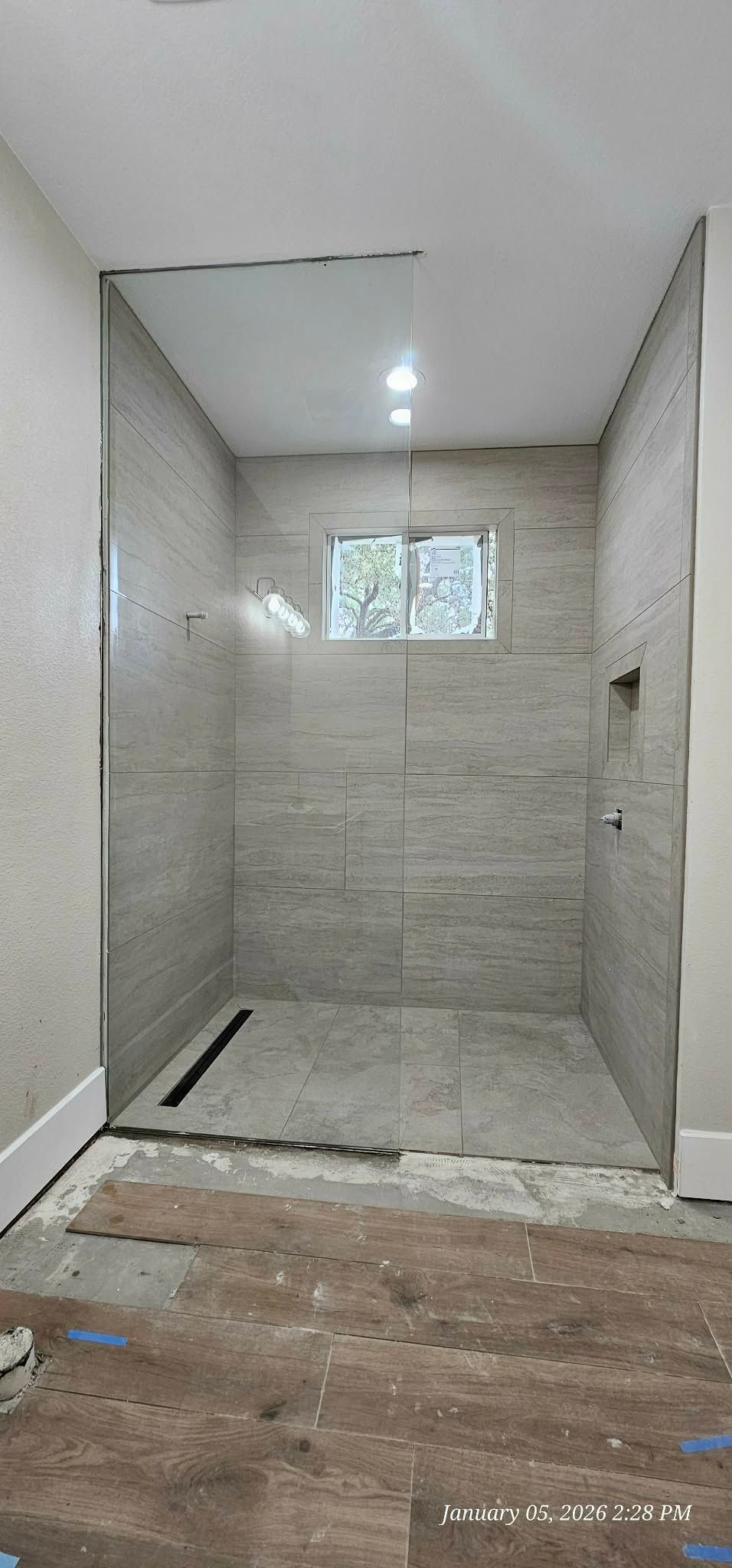 Bathroom under construction, with tiled shower and drain. Window and shower fixtures are installed.