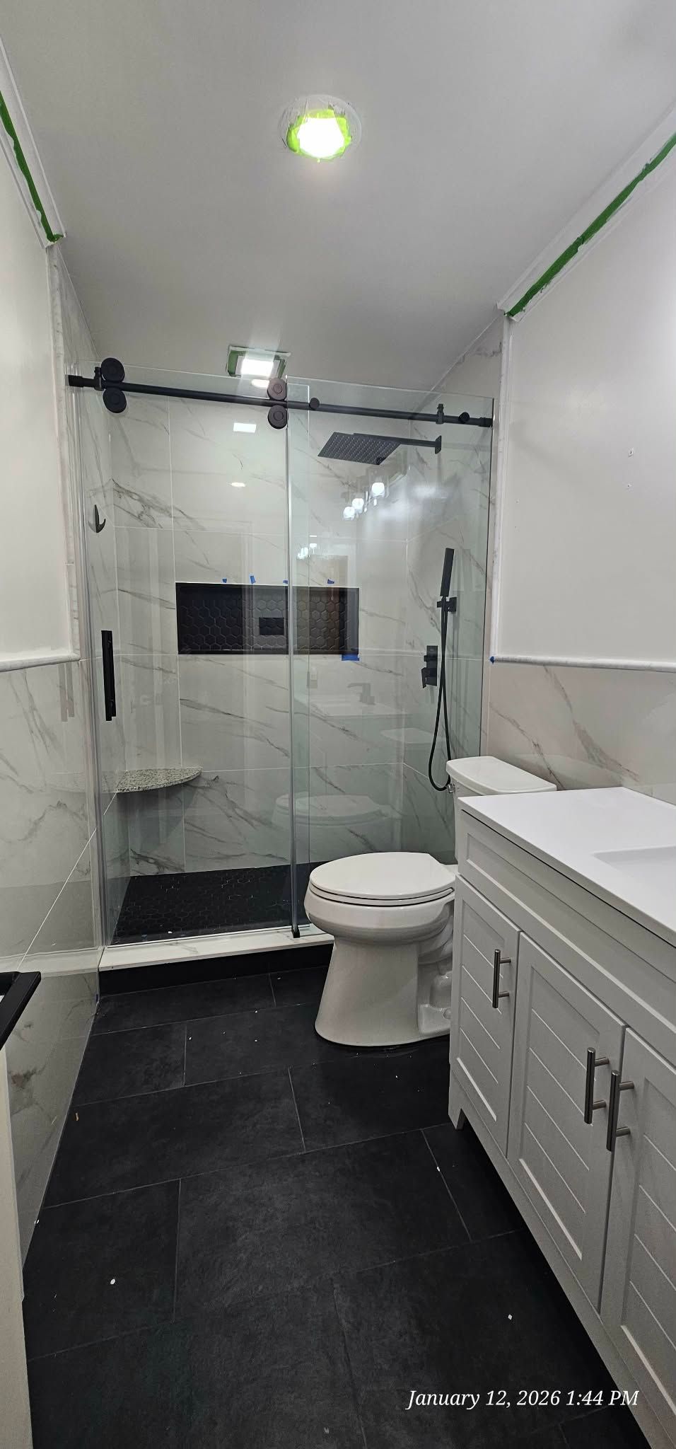 Modern bathroom with white marble shower, black fixtures, and white vanity.