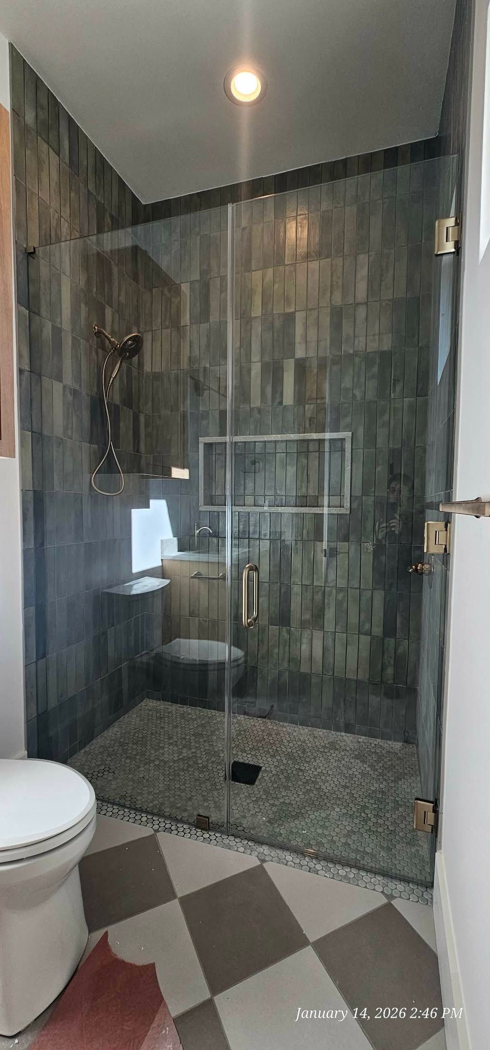 Bathroom with glass shower door, pebble shower floor, tiled walls, and checkered floor.