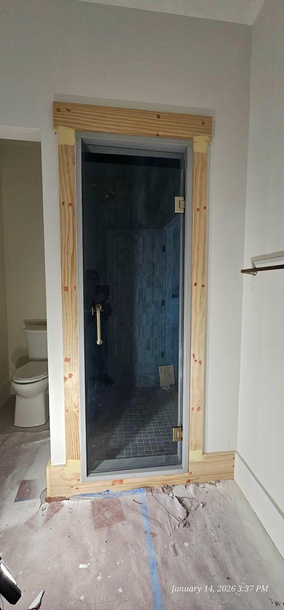 Framed glass shower door in bathroom with wooden trim, unfinished walls and floor.