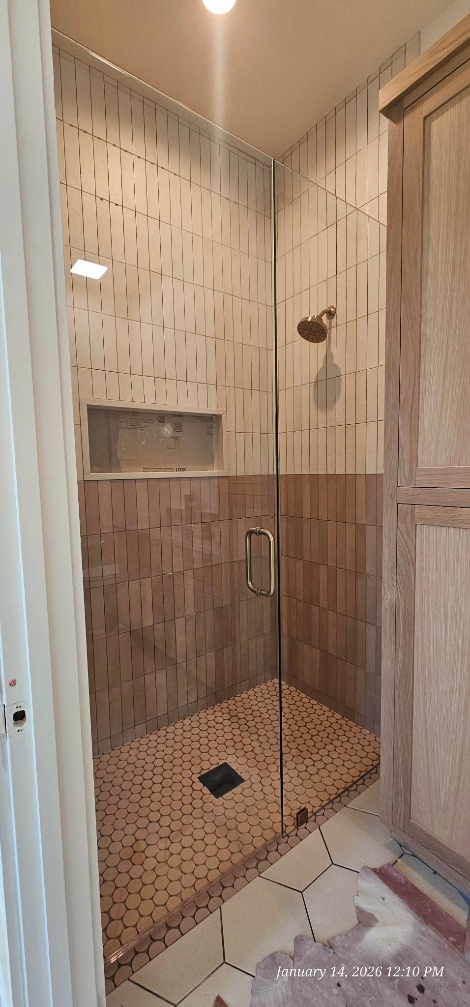 A shower with glass doors, tiled walls and floor, and a showerhead.