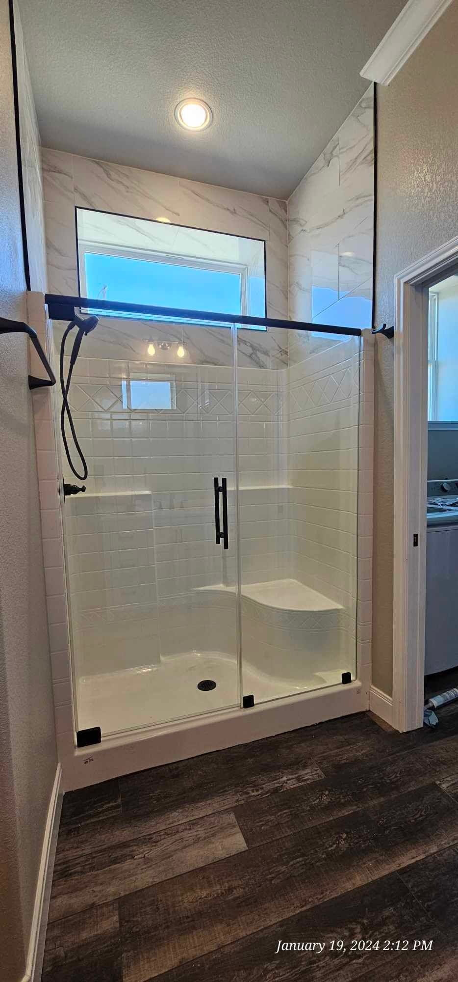 A modern bathroom with a glass shower enclosure and dark wood-look flooring.