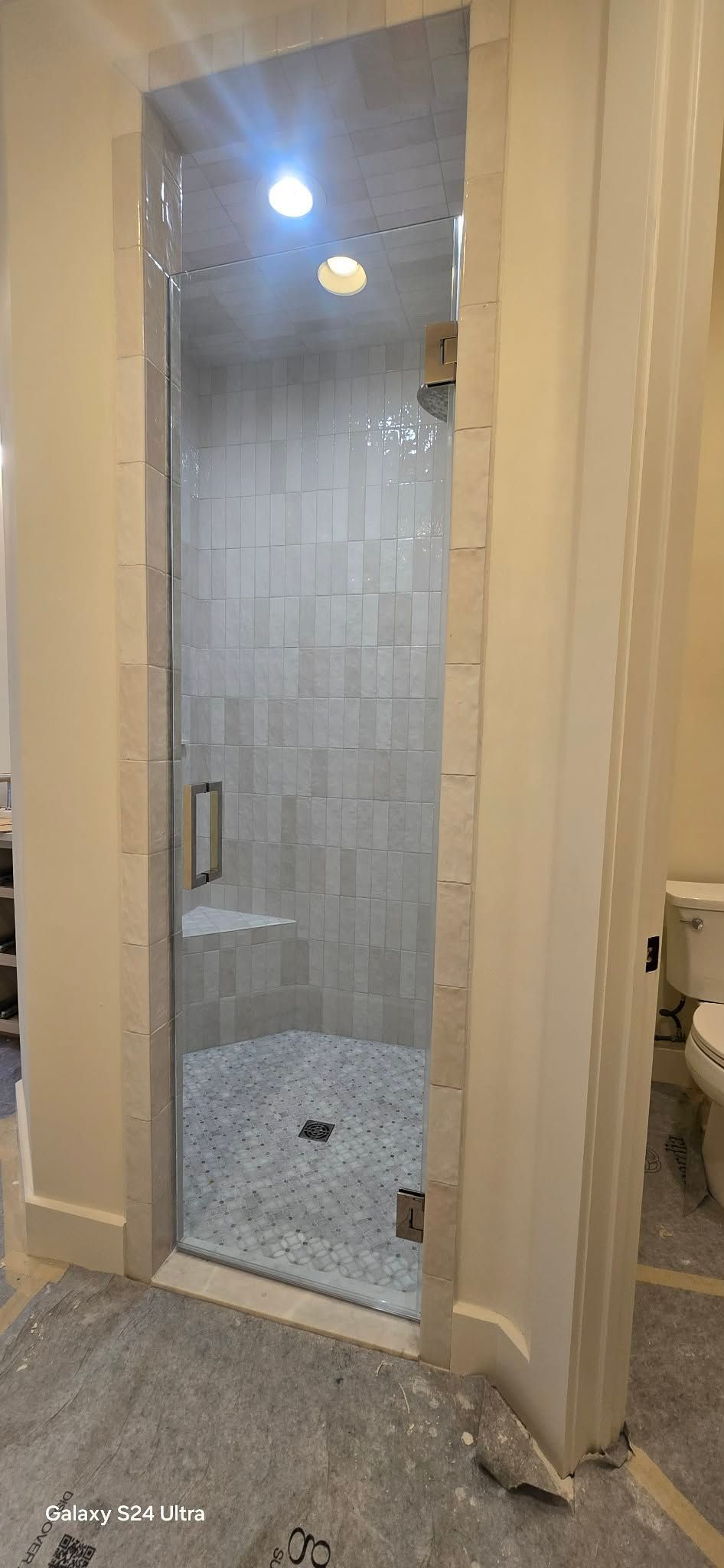 A newly tiled shower with a glass door in a bathroom under construction.