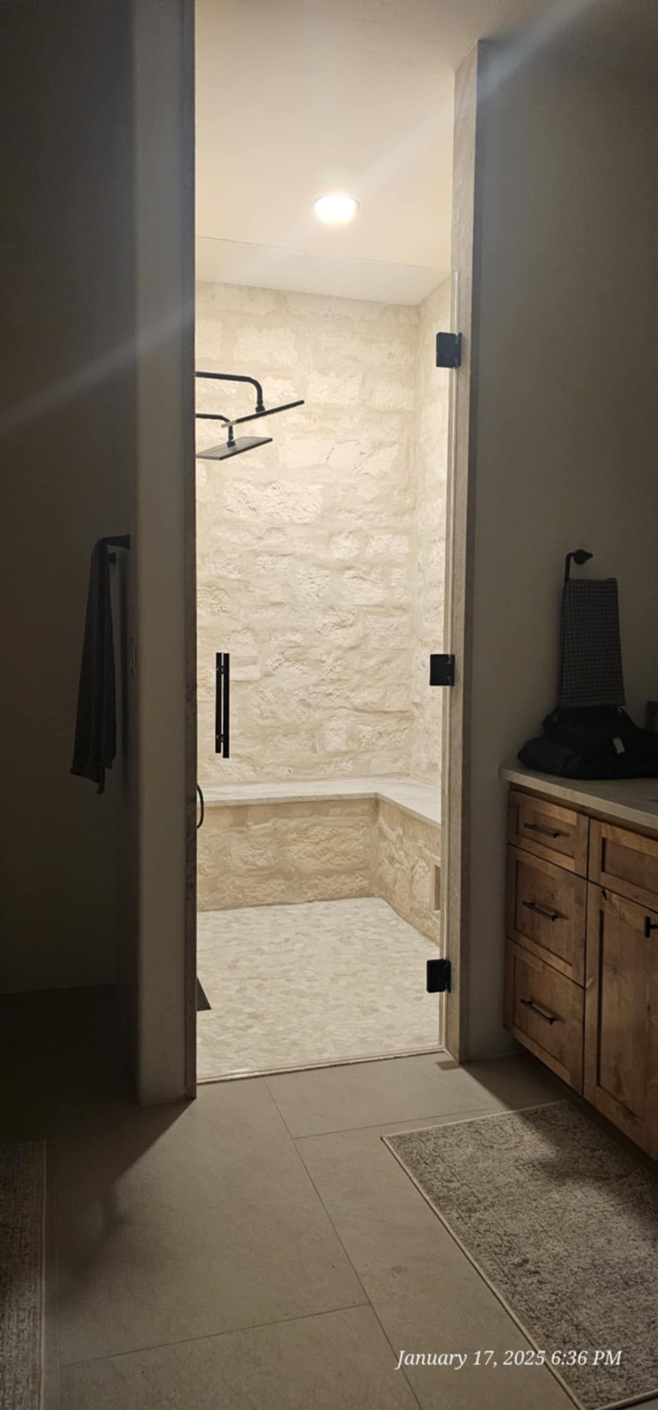 Bathroom doorway reveals a shower with a built-in bench, stone tiles, and a showerhead.