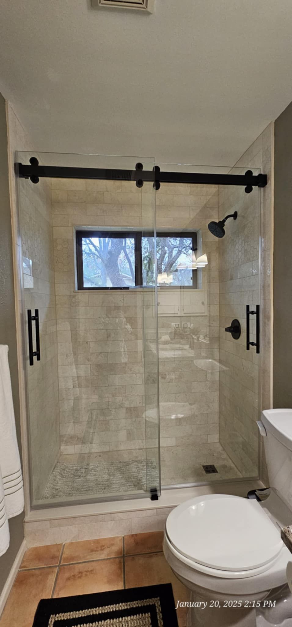 Bathroom with glass shower, black hardware, window, and toilet.