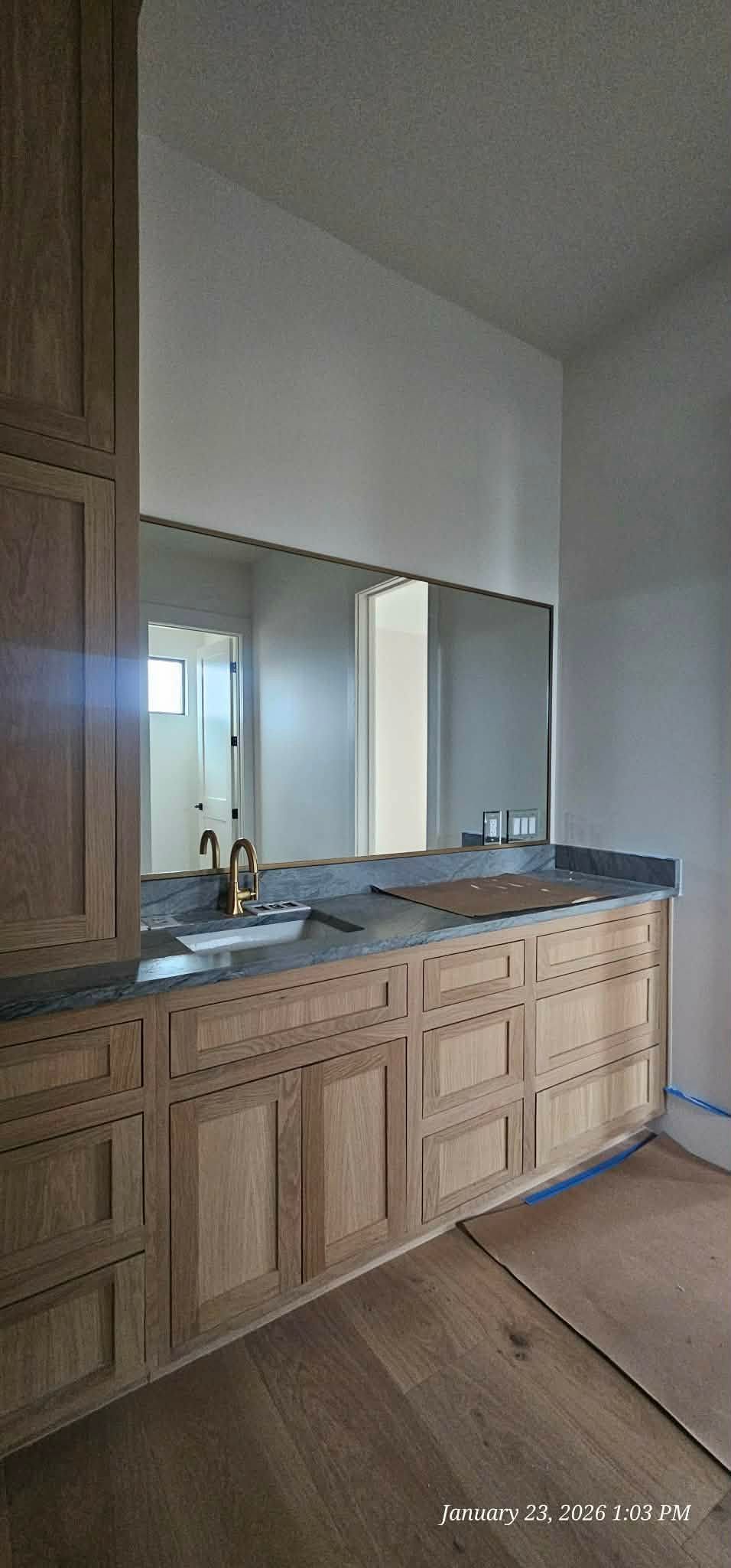 Bathroom with a long mirror above a wooden vanity with a dark countertop.