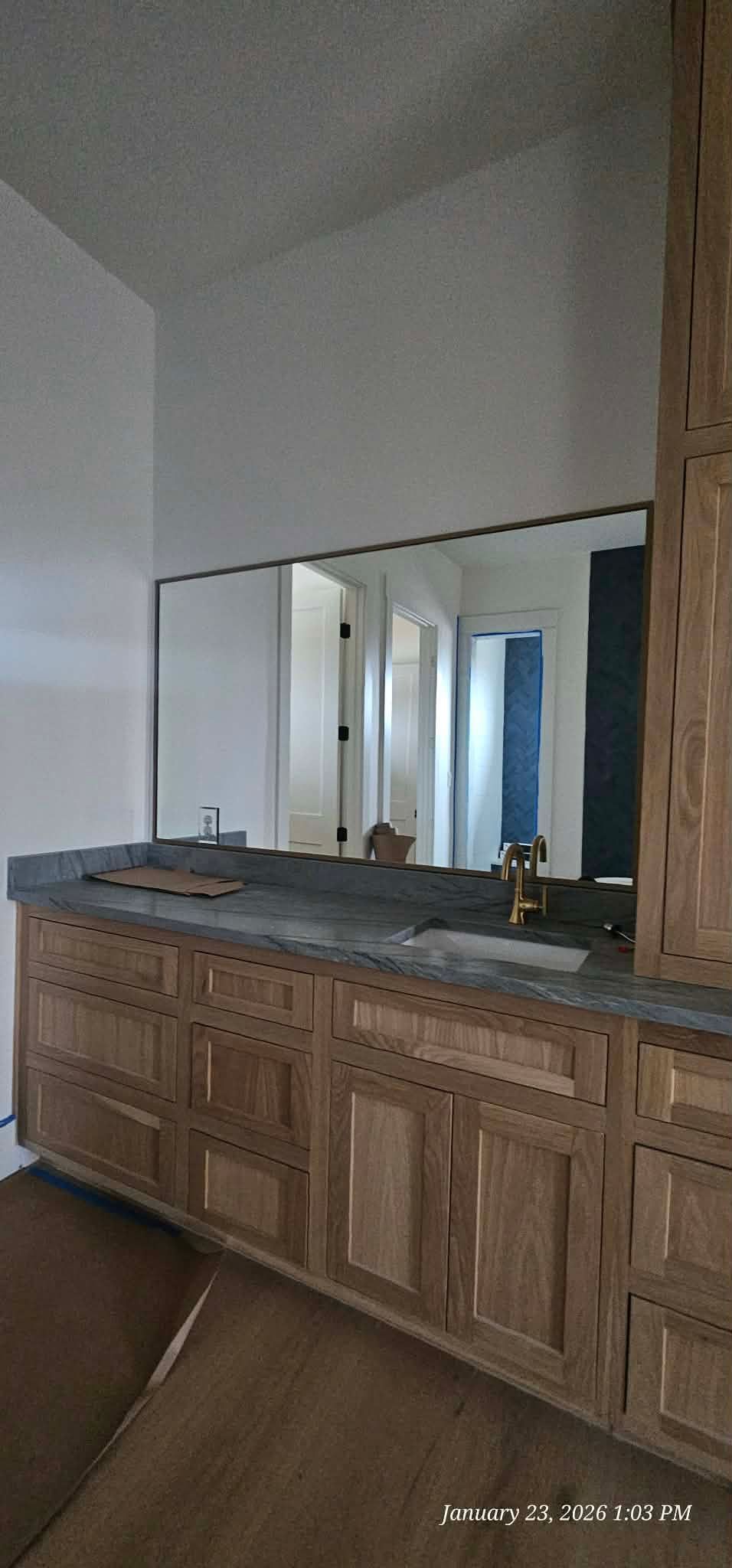 Bathroom vanity with wooden cabinets, dark countertop, and large mirror reflecting the hallway.