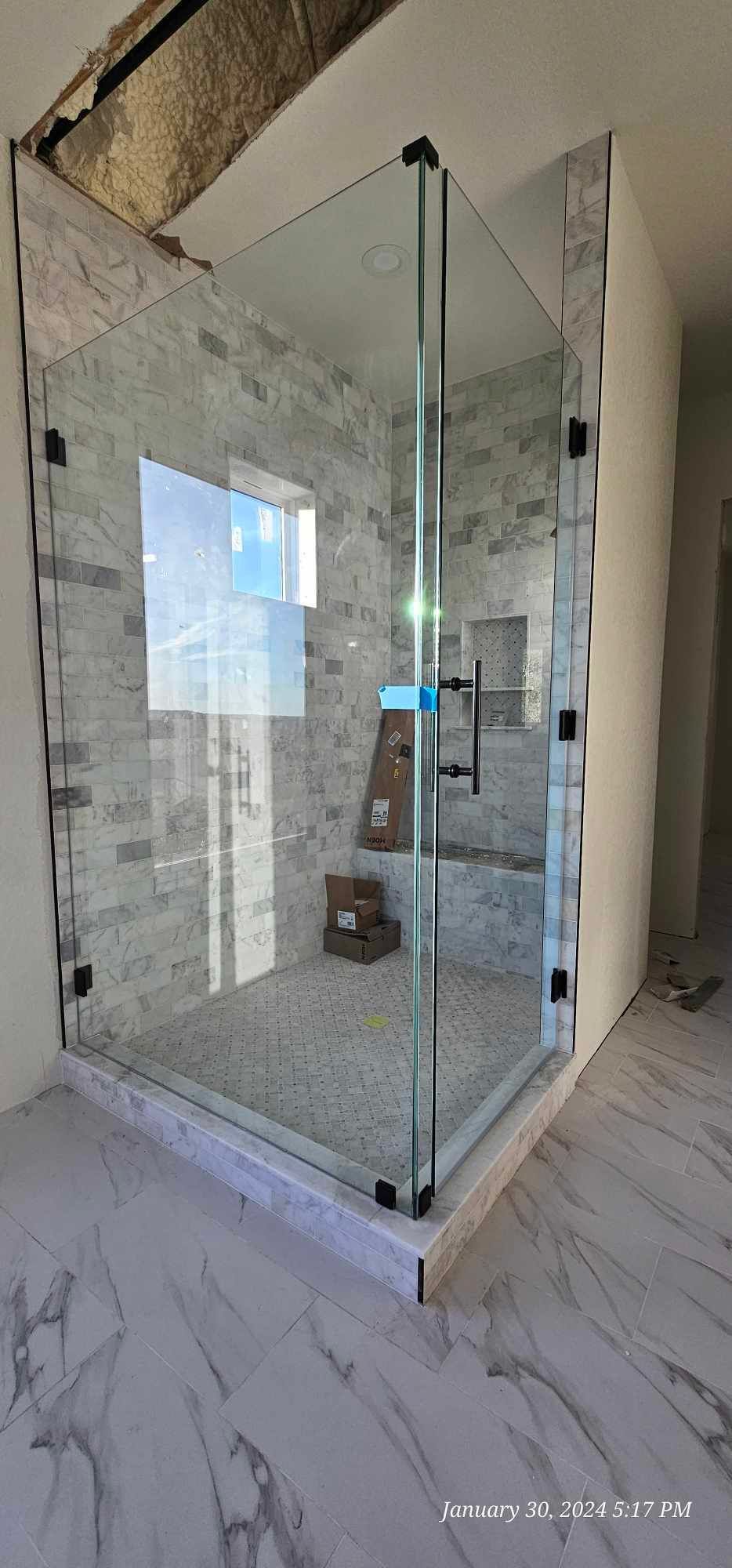 Glass shower enclosure in a tiled bathroom, black hardware.