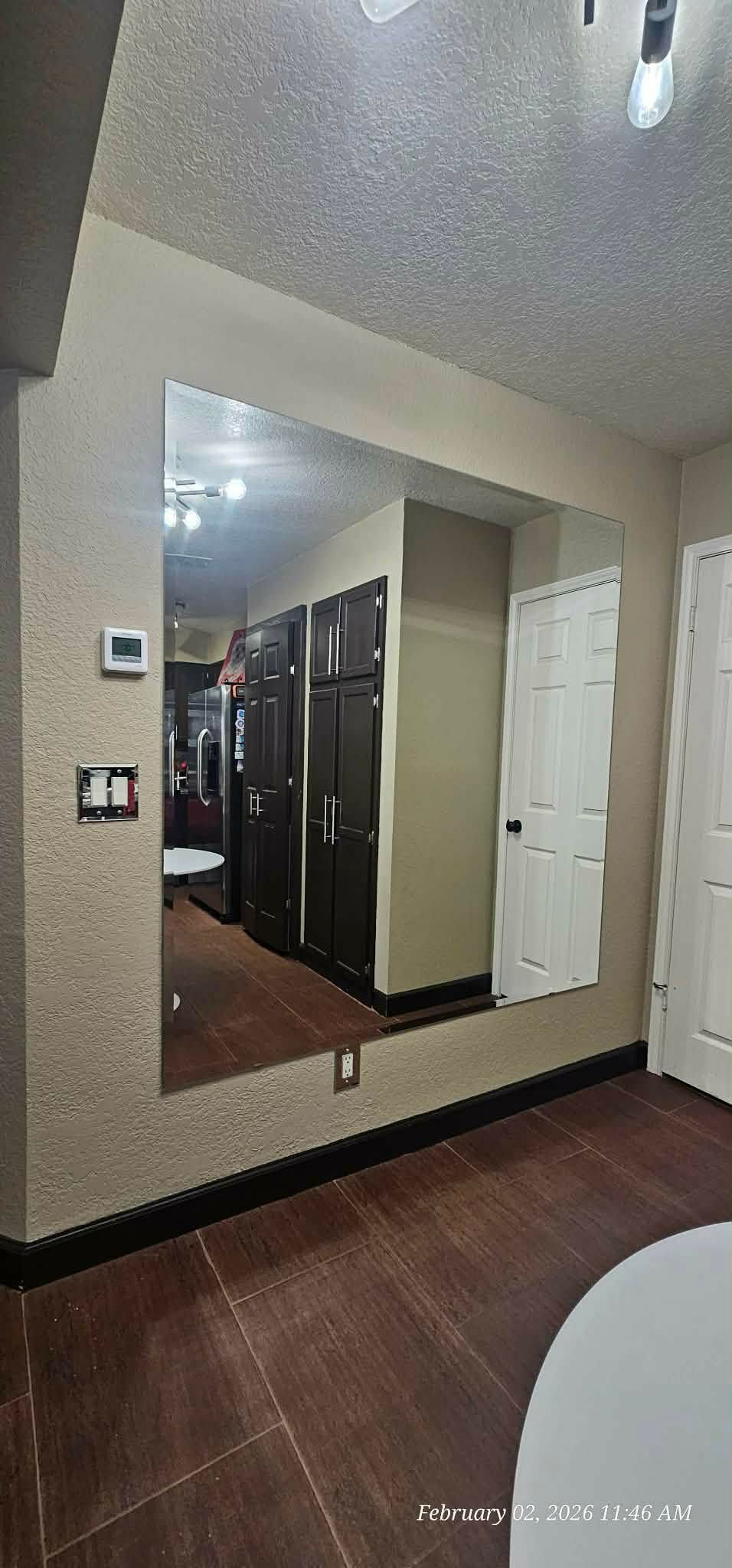 A large mirror on a textured wall reflects a room with dark cabinets and a white door.