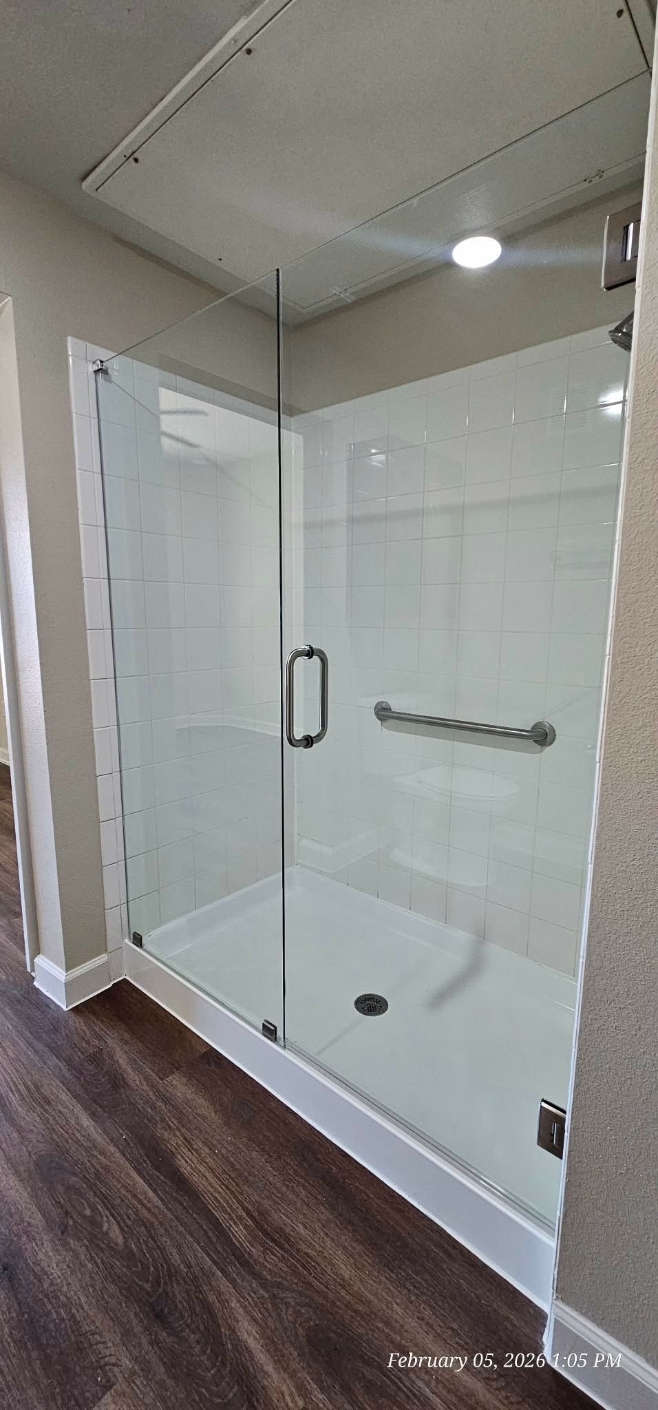 Glass shower enclosure in a bathroom with dark wood-look flooring and white walls.