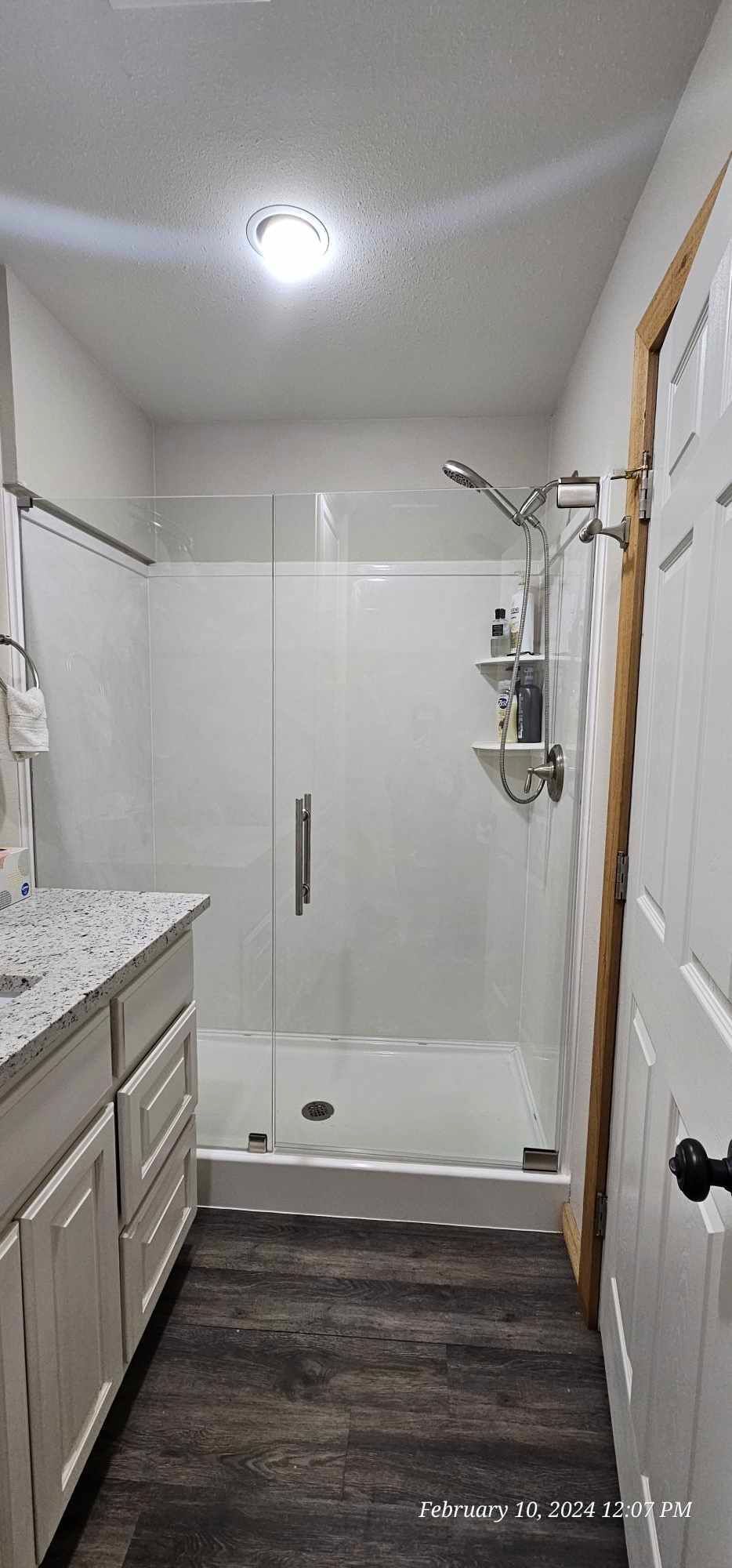 Bathroom with a white-walled shower and vanity, gray countertop and dark wood-look floor.