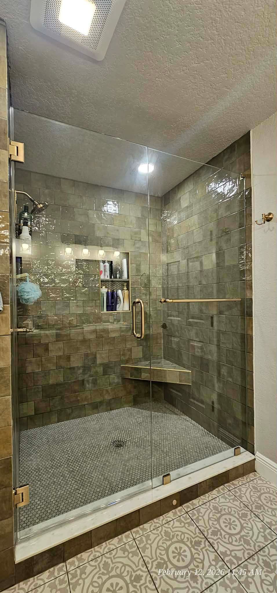 Shower with glass door, stone tile walls and pebble floor. Gold fixtures and built-in bench.