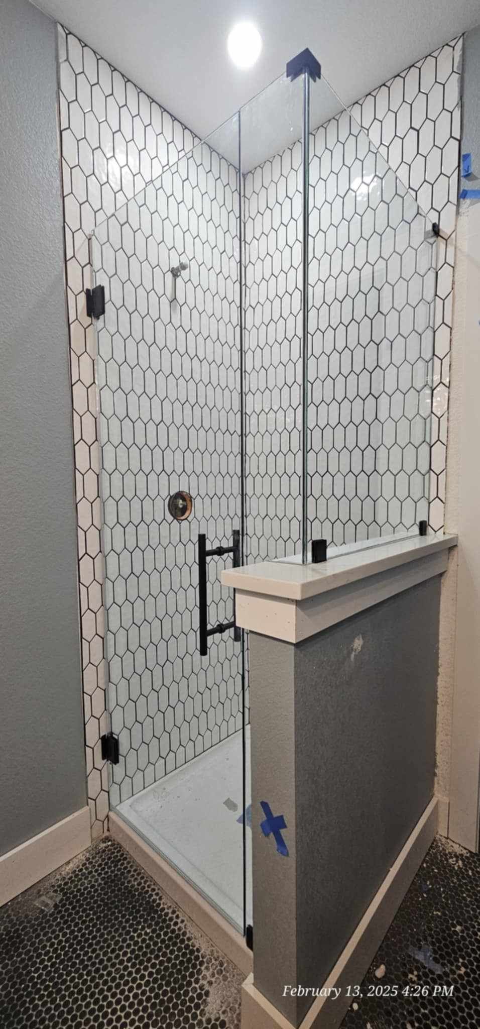 A newly constructed shower with patterned tile, glass doors, and black hardware.