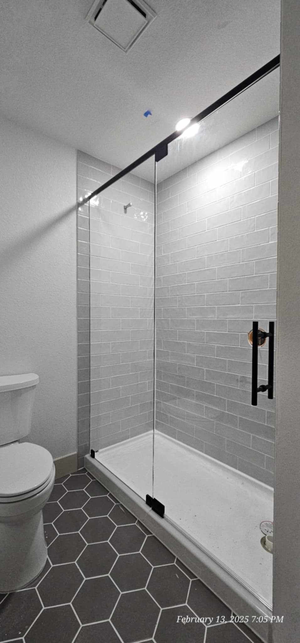 A small bathroom with a glass shower and gray hexagon tile flooring.
