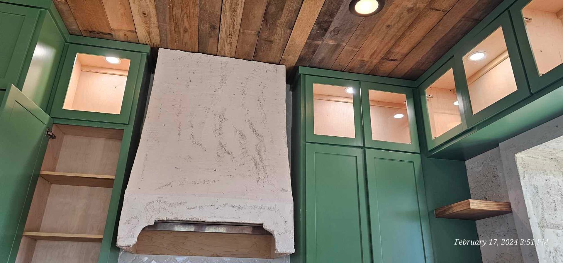Kitchen cabinets in green with wooden ceiling and a cream-colored range hood.