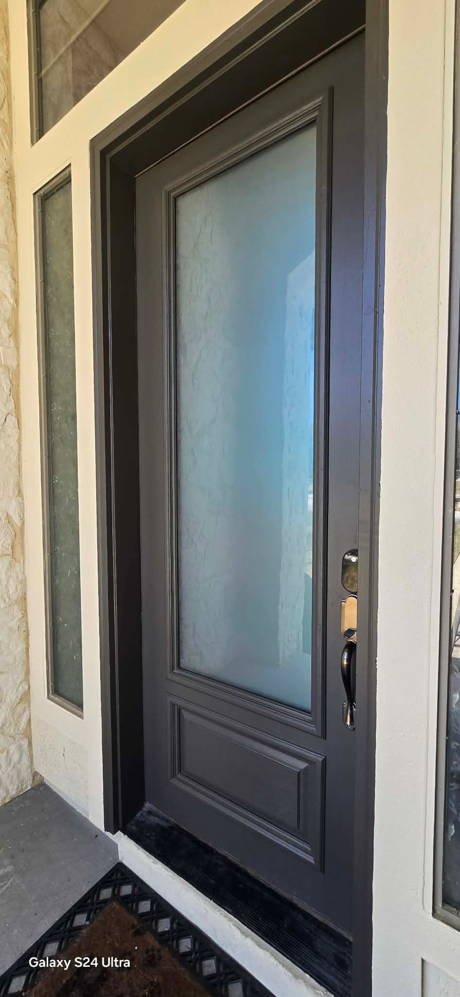 Dark gray front door with frosted glass panel and sidelight, set in white trim.