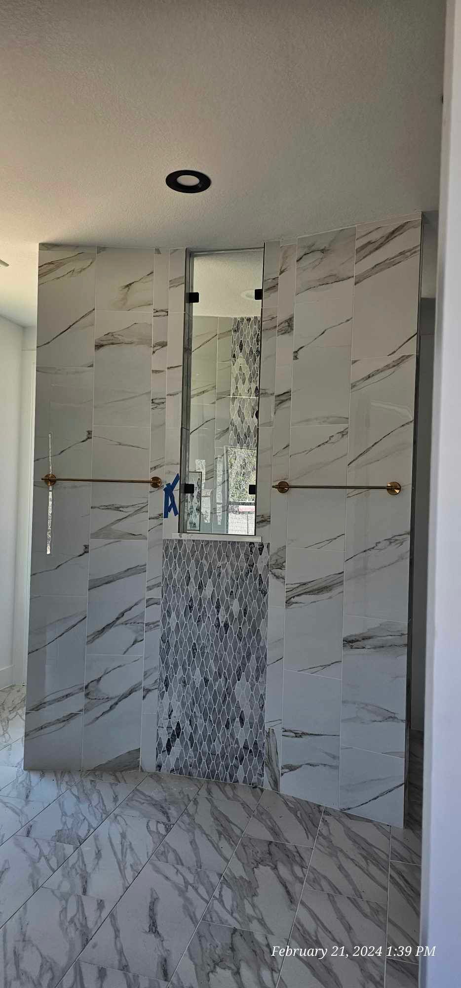 Modern bathroom with marble-patterned tile, glass shower enclosure, and accent wall of mosaic tile.