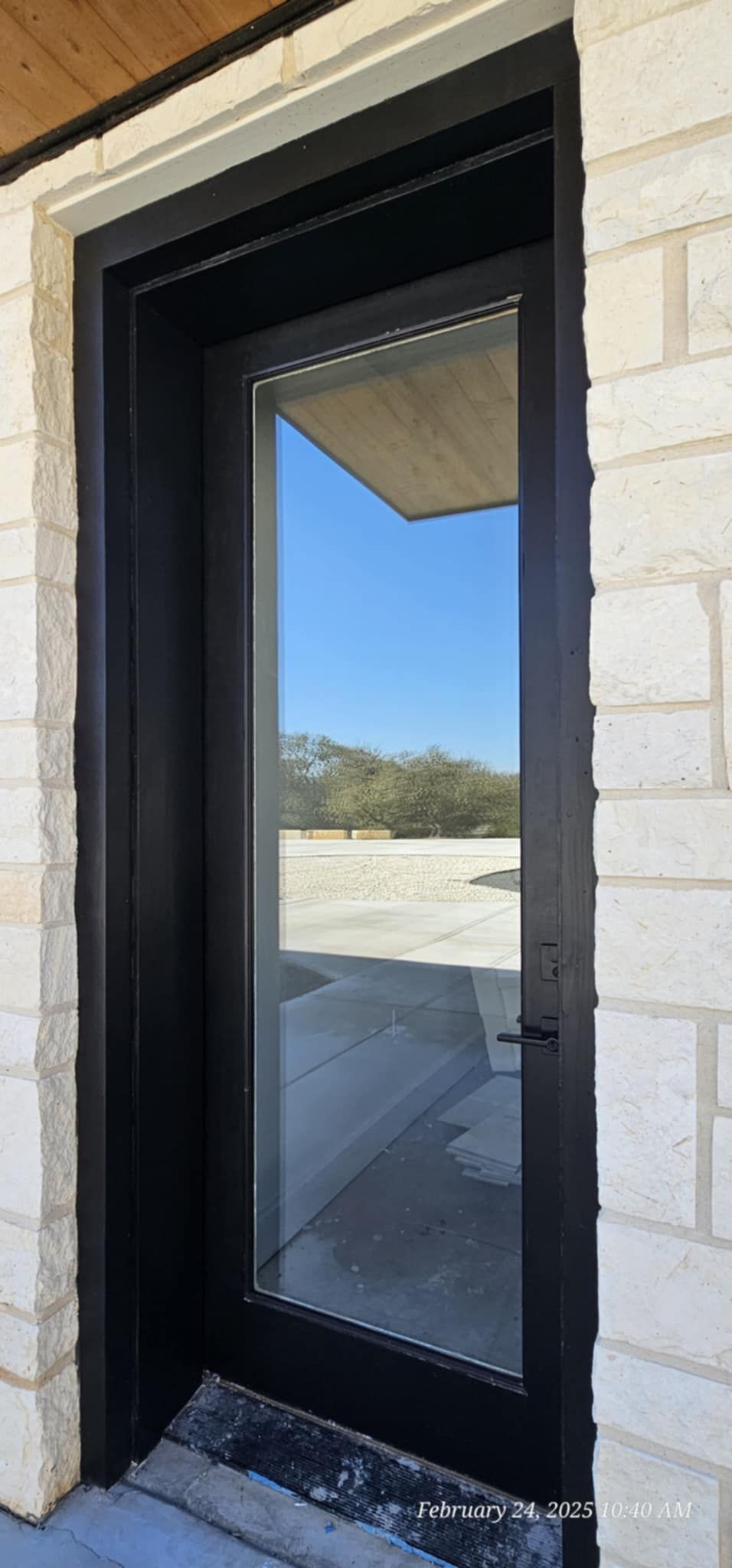 Black framed glass door in a stone wall, reflecting a blue sky and distant landscape.