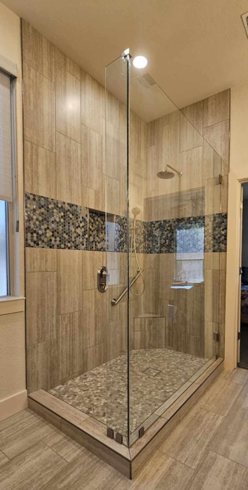 Walk-in shower with pebble floor and glass door. Beige tile walls with accent stripe.