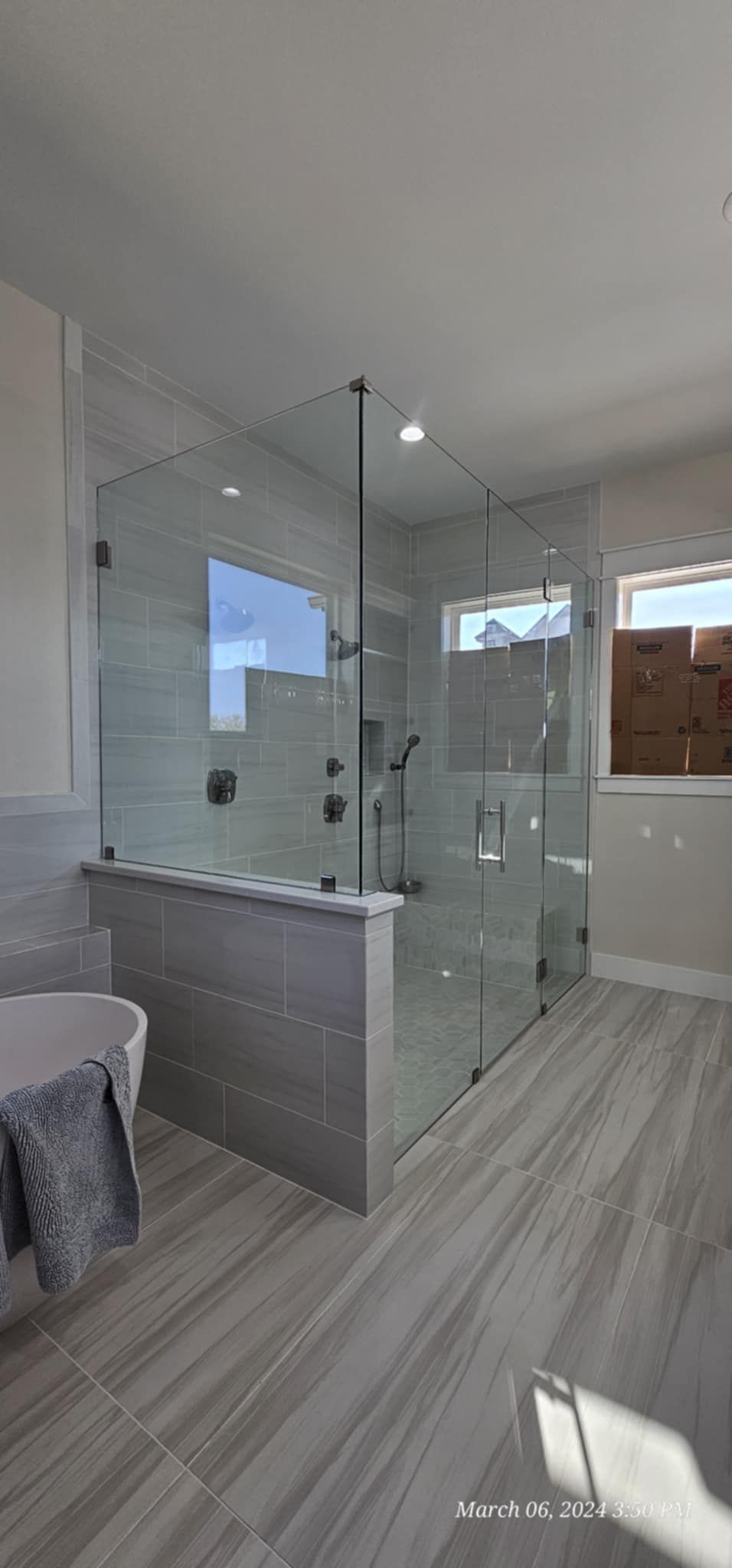 A modern bathroom featuring a walk-in shower with glass doors, gray tiled walls, and a large window.