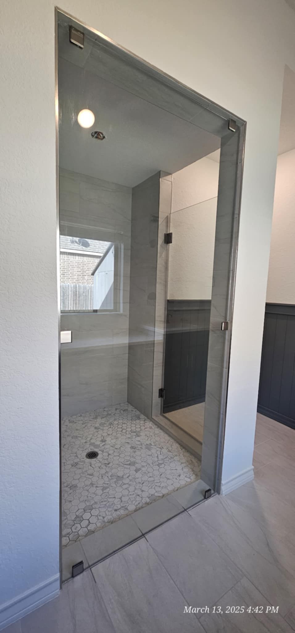 A walk-in shower with a clear glass door. Inside, gray tile, pebble floor, and white walls are visible.