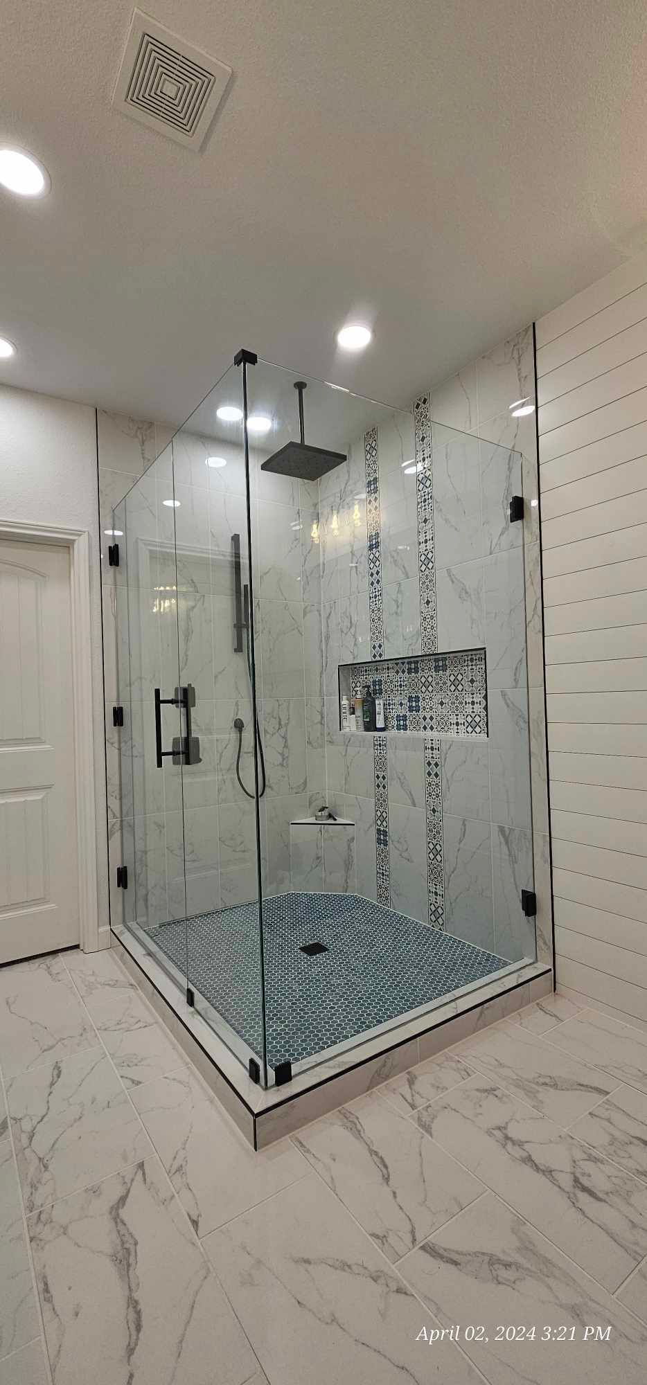 A luxurious shower with glass doors and pebble-tiled floor, featuring white marble walls, and a black showerhead.