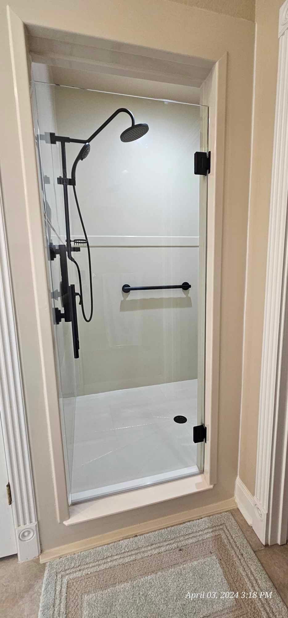 Bathroom shower with glass door and black fixtures. Neutral tones.