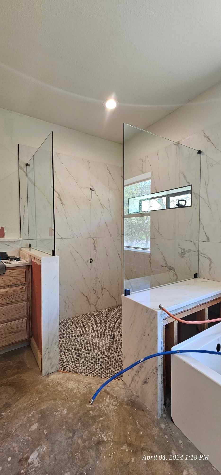 A bathroom under construction with a shower stall, pebble flooring, and marble-like walls.